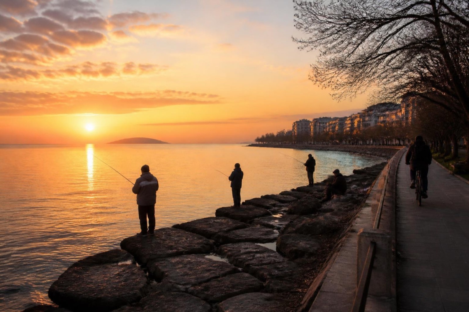 Anglers on a rocky shore and a cyclist on the path beside it at sunrise, with a faint low island far across the water